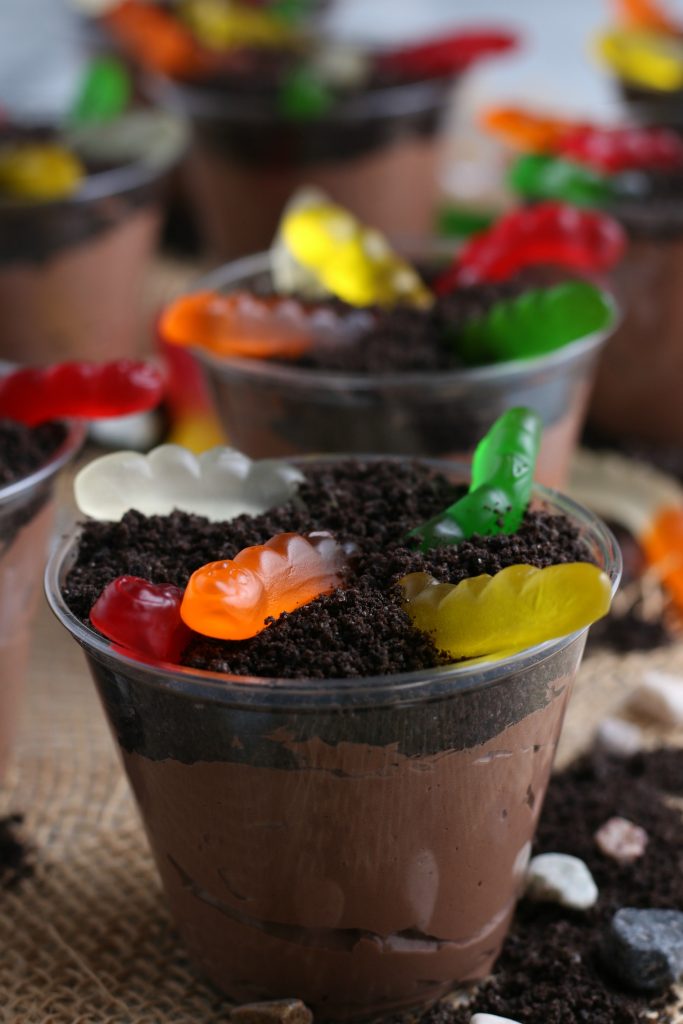 A close up of a dirt cup with pudding. Gummy worms peek out the top of the cup.