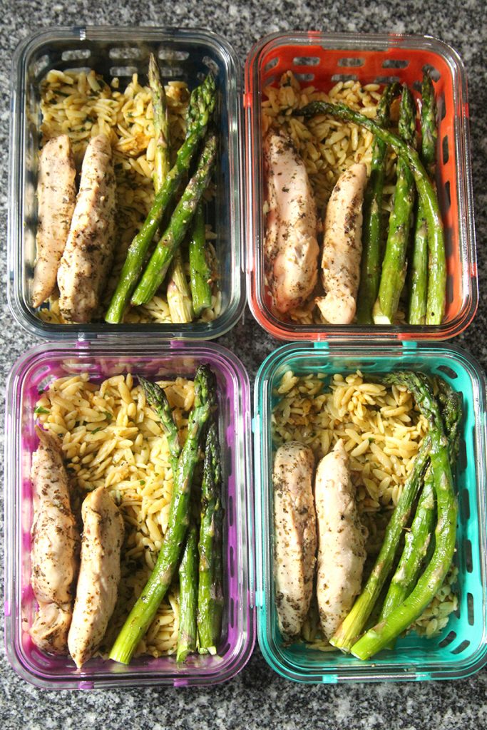 Four colorful glass meal prep bowls are shown. They are all filled with orzo topped with chicken and asparagus.