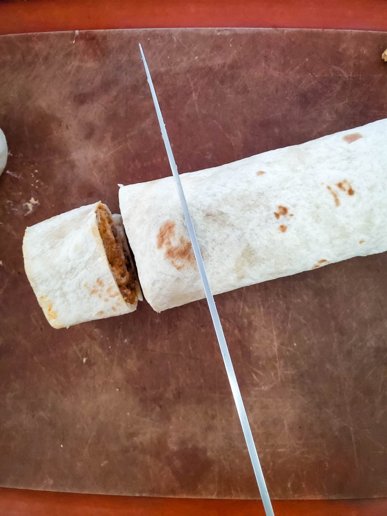 A sharp knife cuts Cheesy Taco Pinwheel pieces from a log.