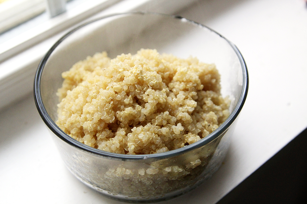 A glass bowl filled with cooked quinoa is shown on a windowsill.